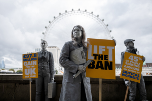 A photograph of a woman spray painted silver to look like a statue holding a lift the ban poster.