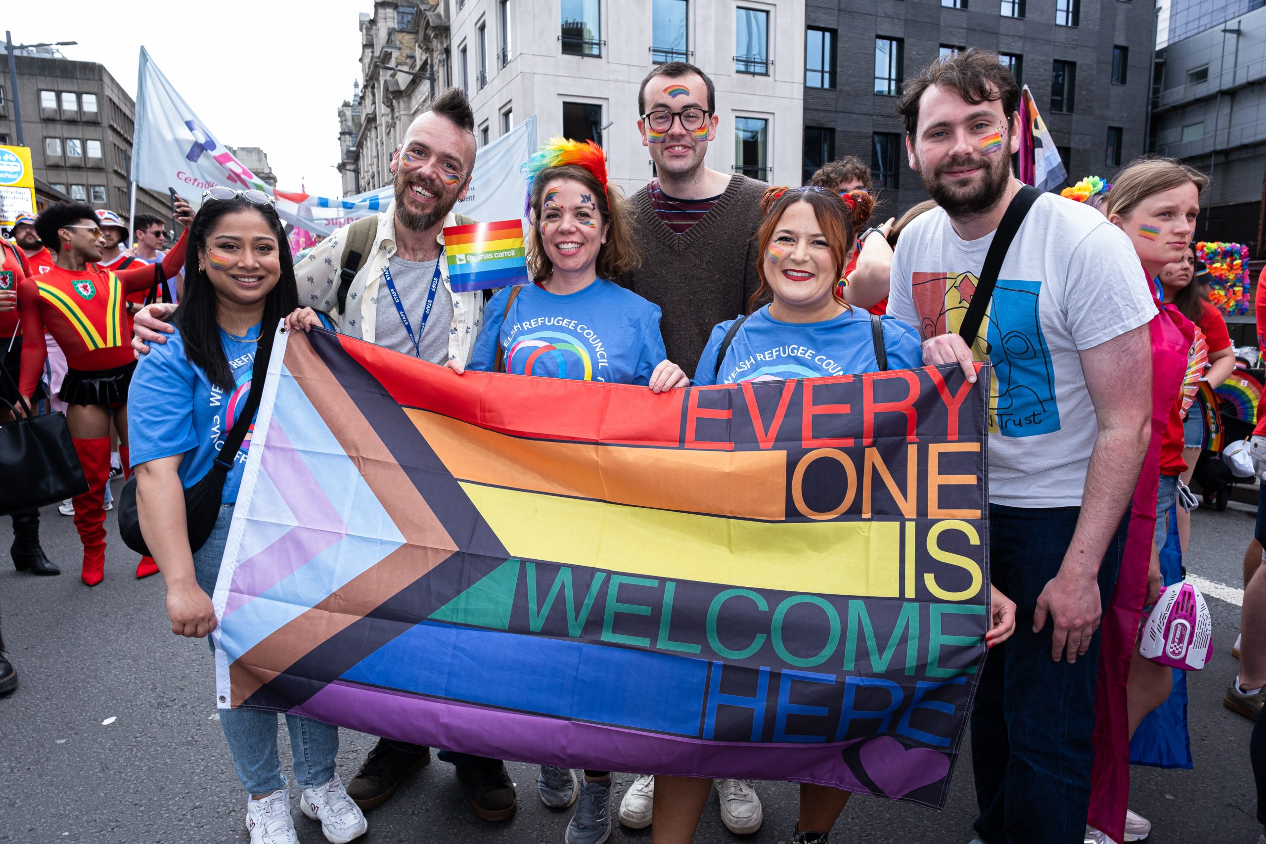 People holding a rainbow banner reading Everyone is welcome at a Pride march
