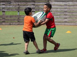 Two children sharing a large rugby ball.