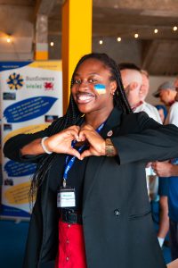 Woman making a heart with her hands. She has the Ukrainian flag painted on her cheek.