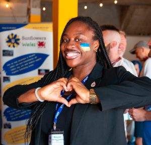 Woman making a heart with her hands. She has the Ukrainian flag painted on her cheek.