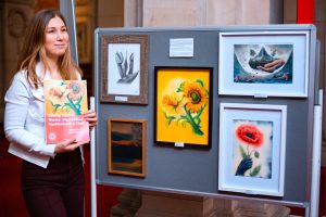 Woman standing next to artwork at event to commemorate invasion of Ukraine. 