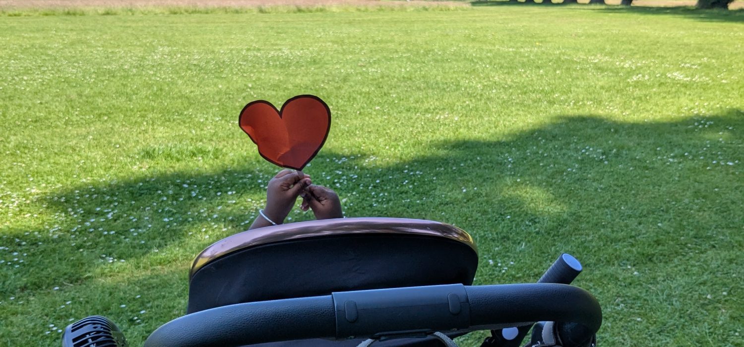 Child holding a orange heart above a buggy.