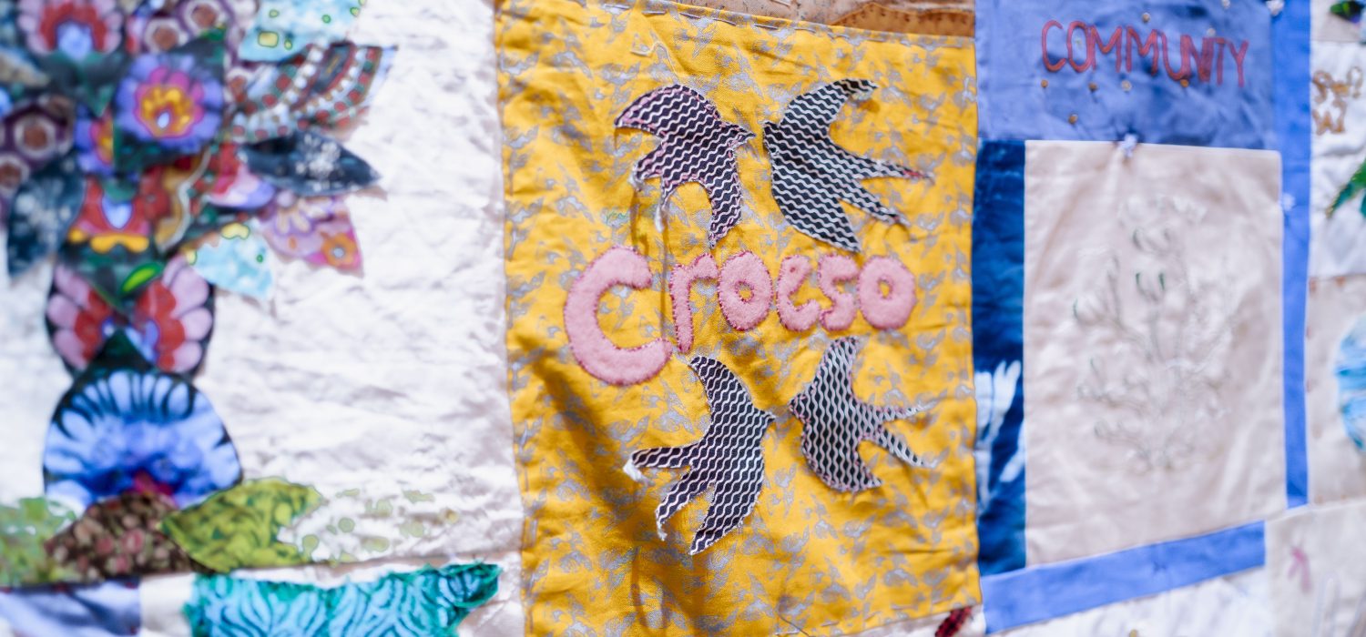 A colourful hand-made quilt from sanctuary seeking communities. Panel reads 'Croeso', the Welsh word for welcome.