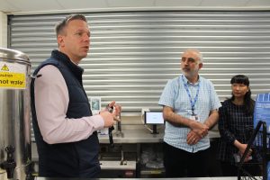 Man stood talking to two other people in a kitchen. 