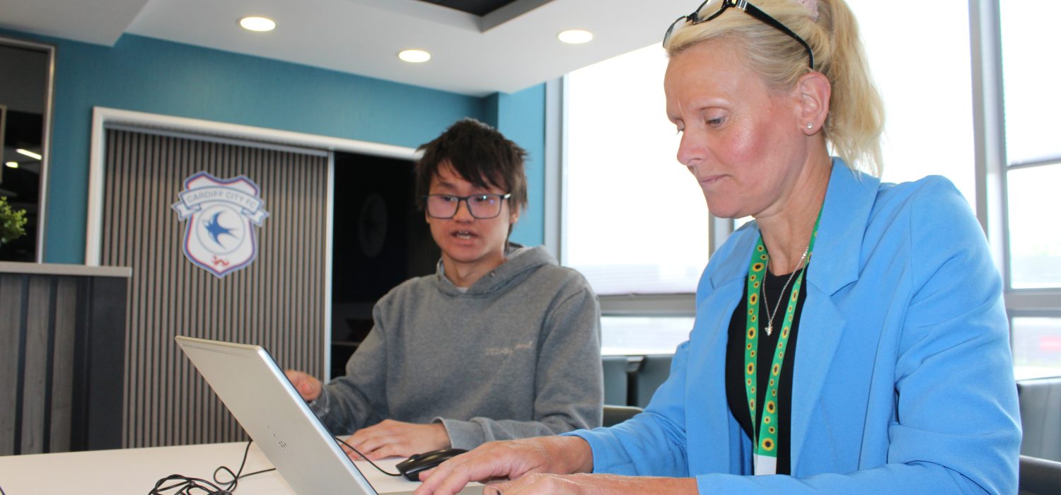 Woman typing at a laptop sat next to a person.