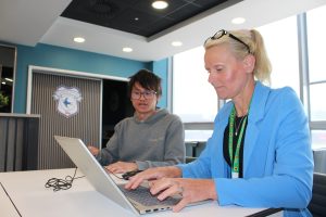 Woman typing at a laptop sat next to a person.