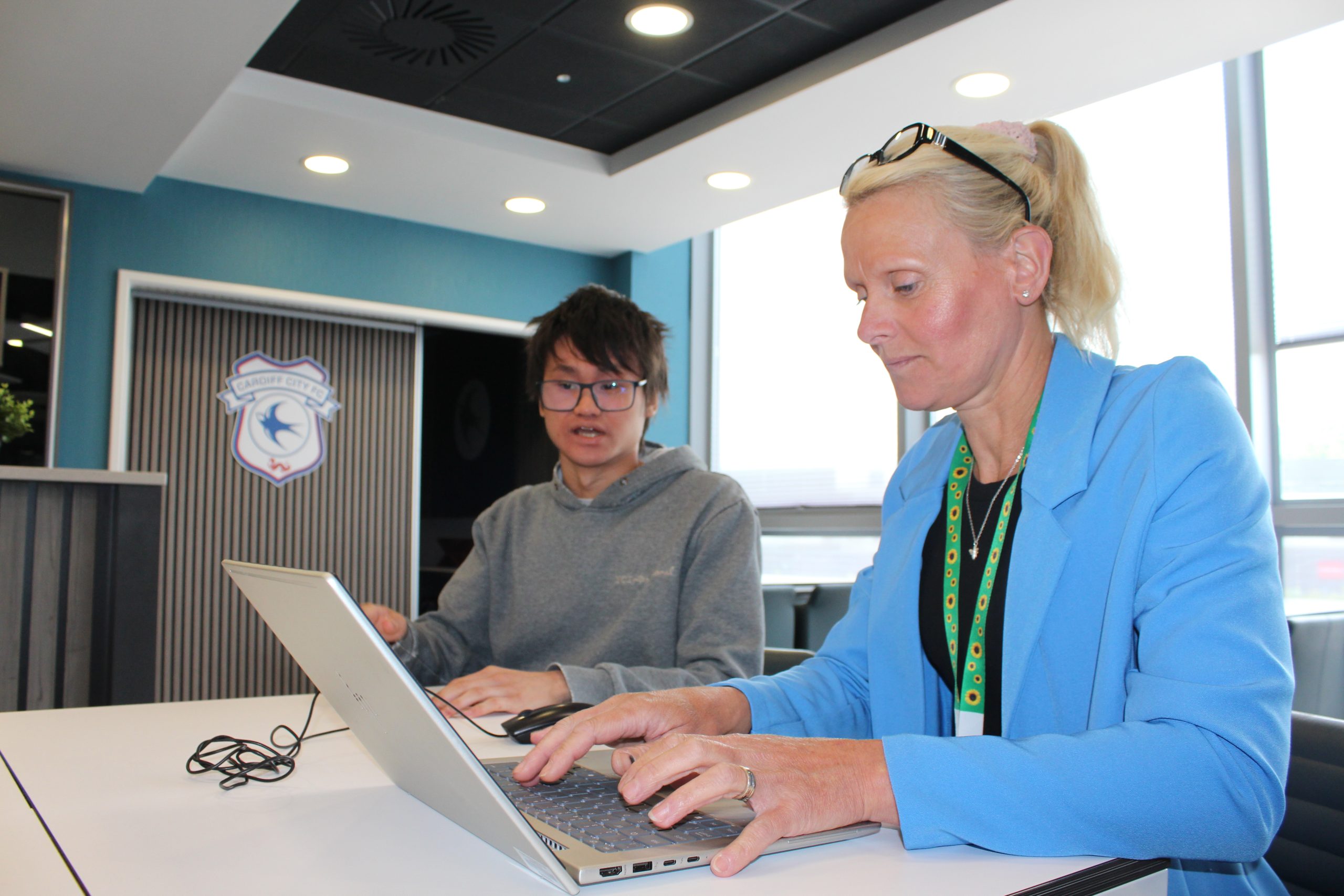 Woman typing at a laptop sat next to a person.