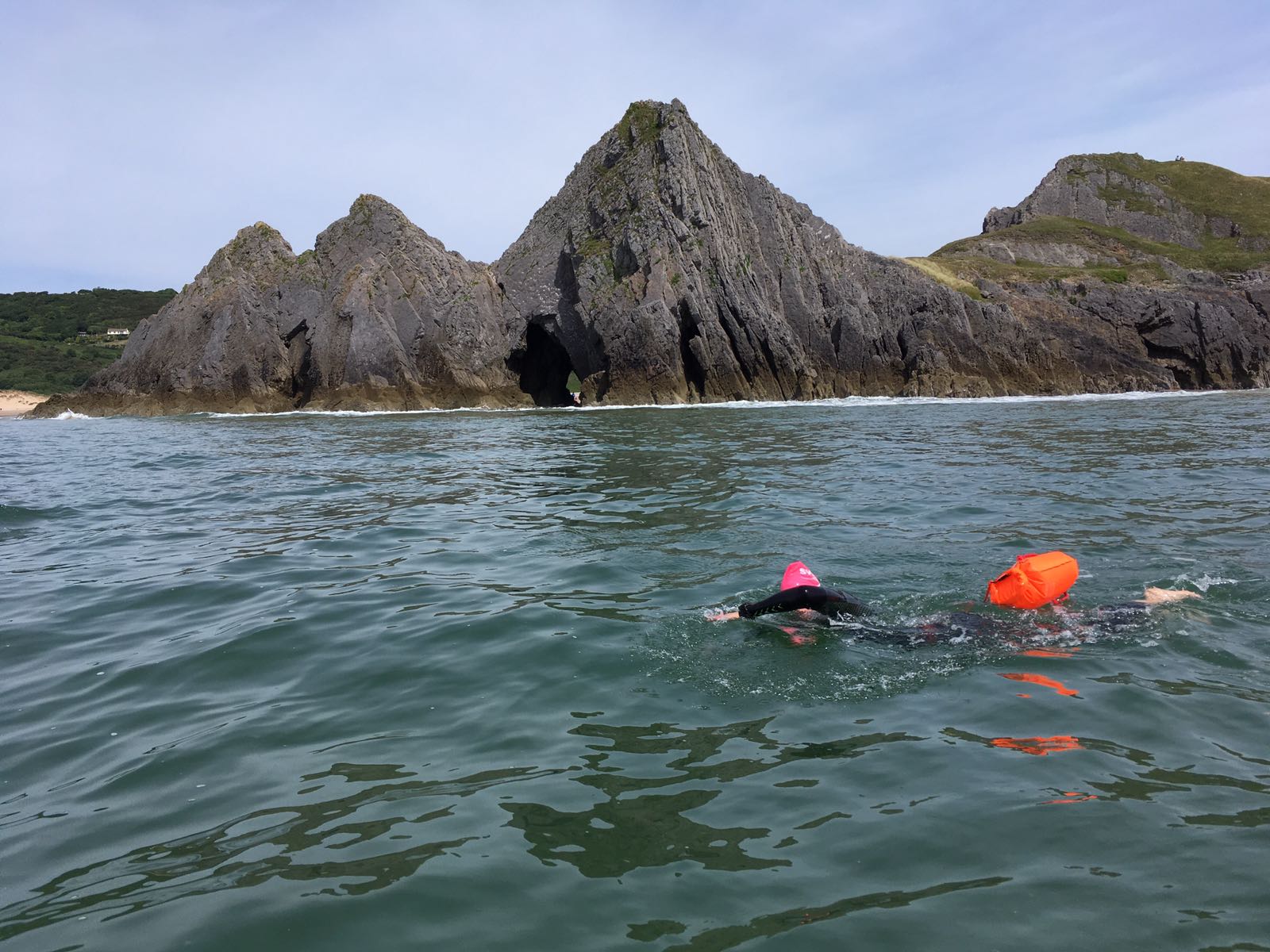 A swimmer in open water beside rocky cliffs