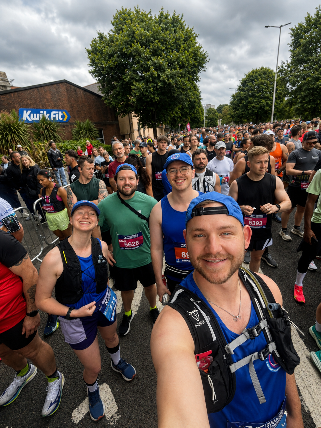 A group of smiling runners in a crowd at the start of a race