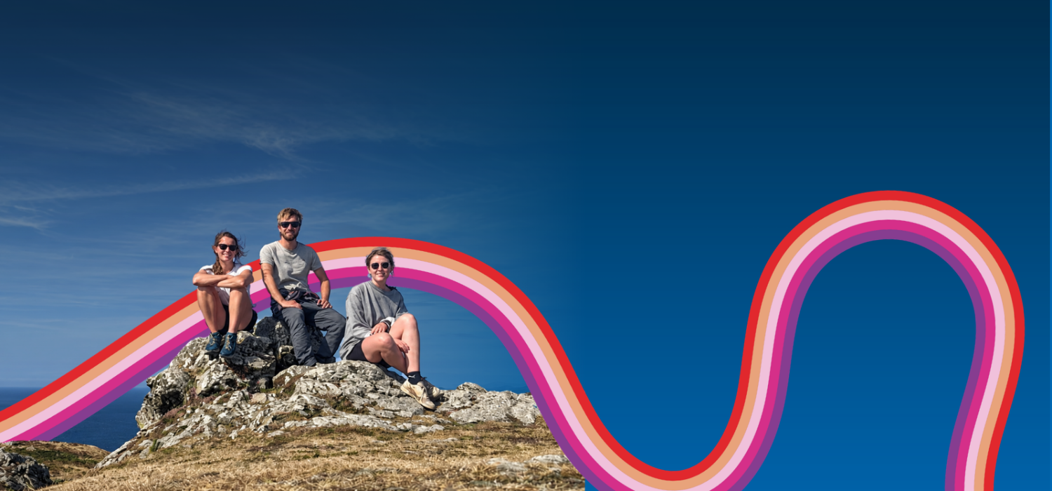 Three people sit on a rock at the top of a mountain smiling at the camera